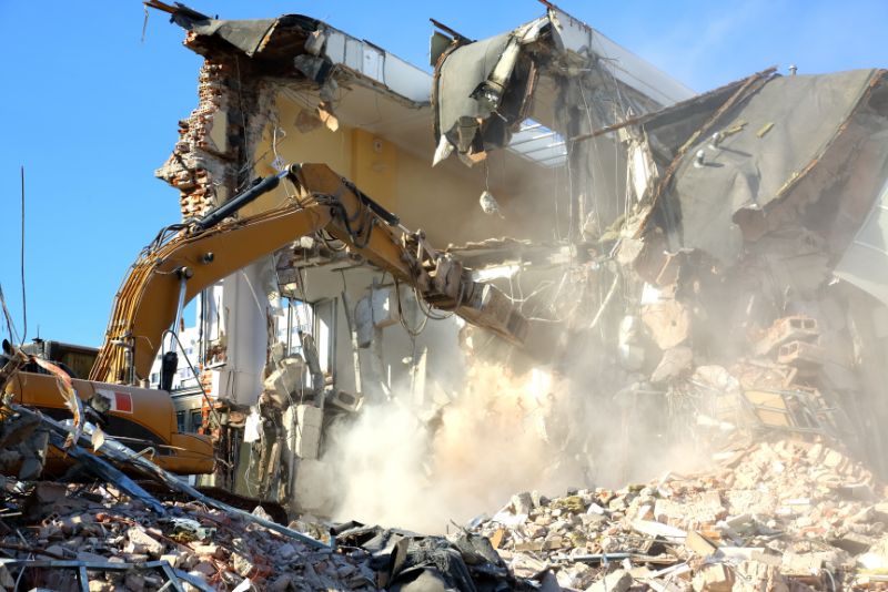 a yellow excavator demolishing a building